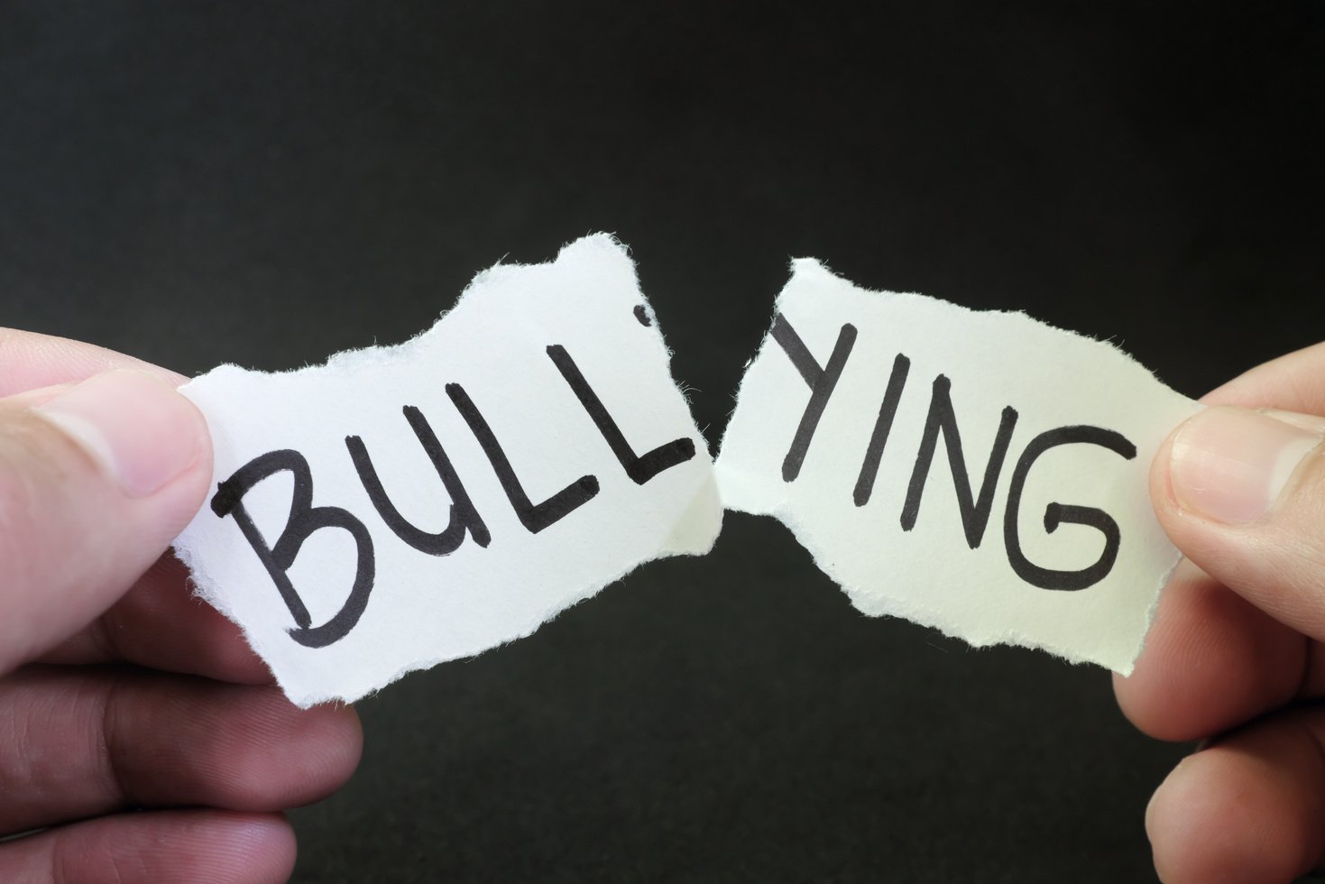 Fight and stop bullying concept. Hand tearing paper with word bullying in dark black background.